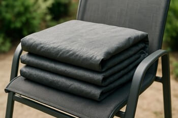 Folded outdoor furniture cover lying beside a low bench on the grass