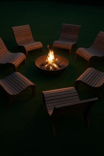 Curved outdoor chairs forming a ring around a low fire bowl on trimmed grass
