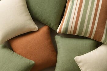 Stack of outdoor cushions in muted green and sand tones on a bench