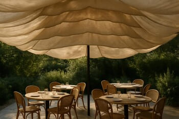 Daybed beneath layered fabric canopies with soft dappled light on the lawn