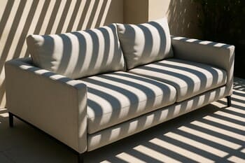 Outdoor sofa under a pergola casting striped shadows on the cushions and grass